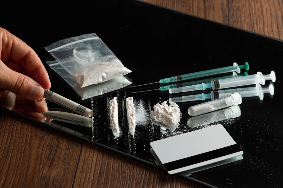 Un homme tient un tube de dollar près des seringues et de petits paquets de drogues différentes