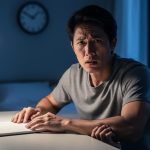 Person sitting at a desk at night with tense posture and a worried expression, symbolizing chronic anxiety and sleep disruption.